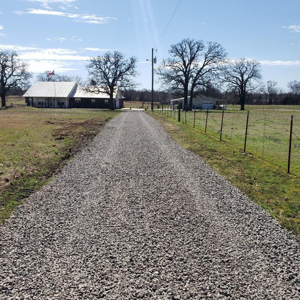 A gravel road leading to a house in the middle of a field.