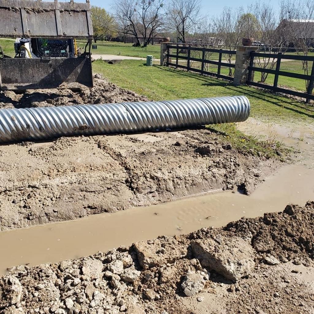 A large metal pipe is sitting in the middle of a muddy field.