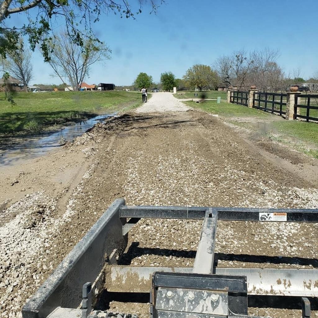 A tractor is driving down a dirt road with a fence in the background
