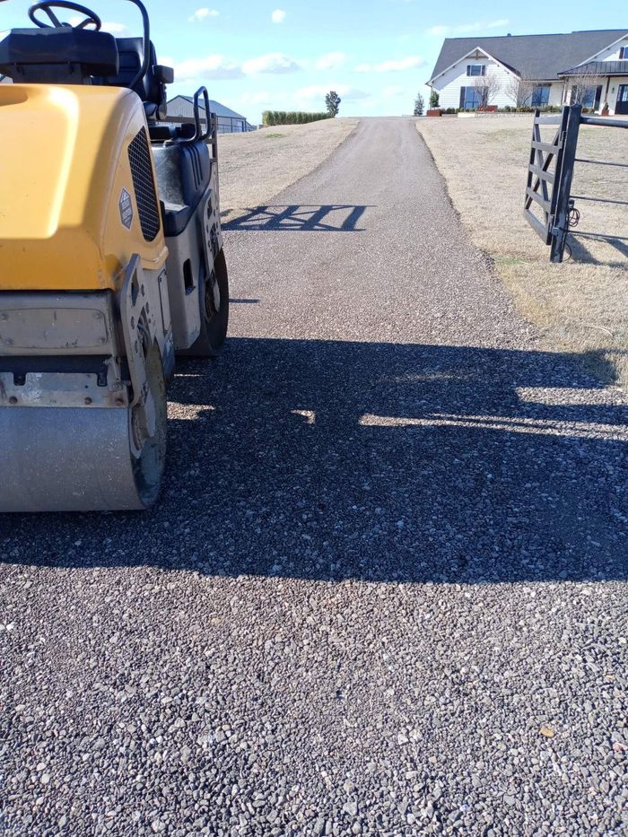 A yellow roller is rolling gravel on a road.