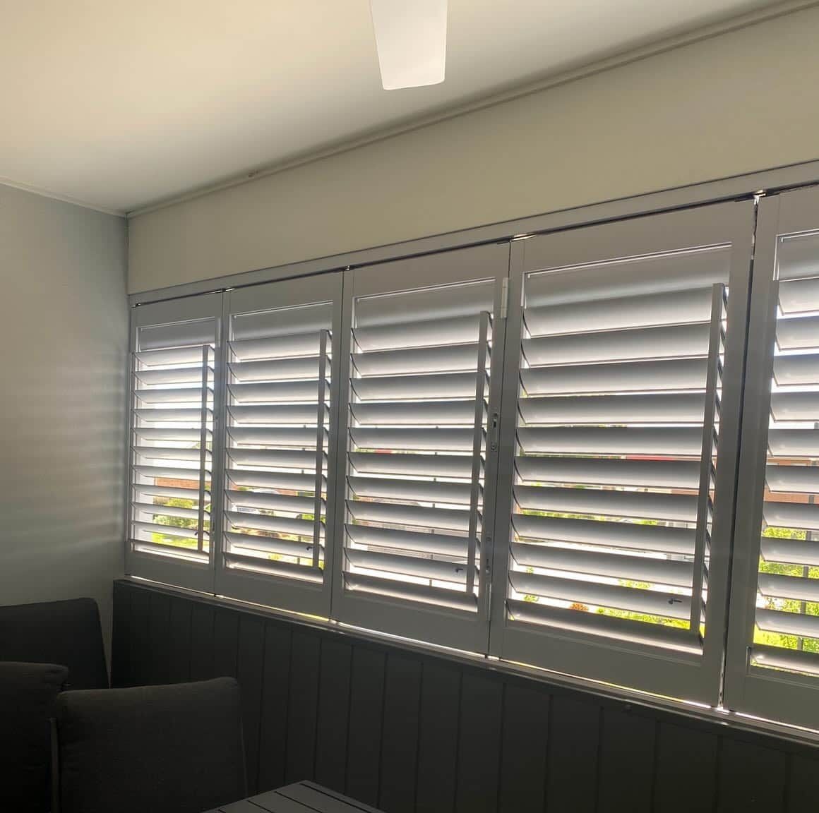 A Living Room with A Lot of Windows with Shutters on Them — Douglass Blinds & Security Screens in Canberra, NSW