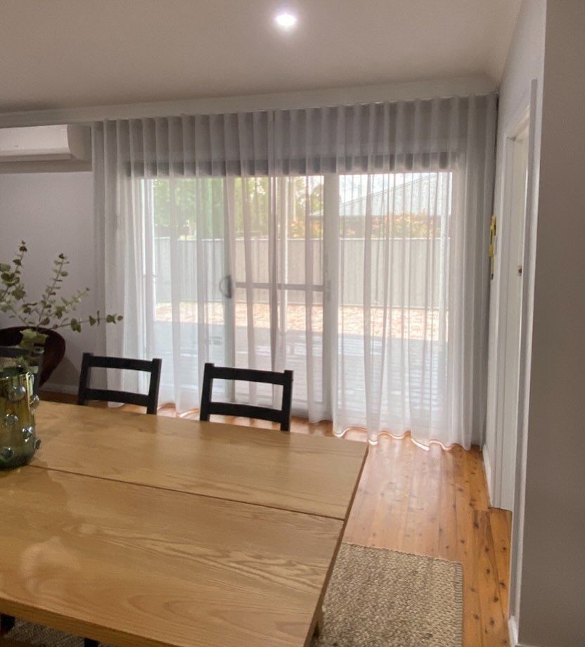 A Dining Room With a Wooden Table and Chairs and White Curtains — Douglass Blinds & Security Screens in Goulburn, NSW