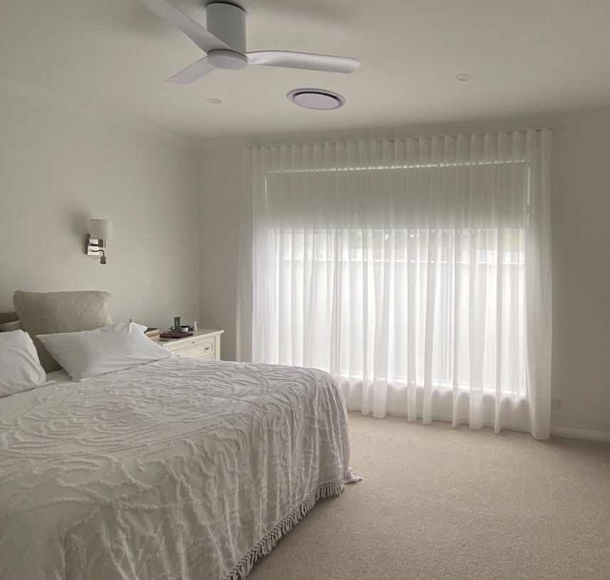 A bedroom with a bed, a window and curtains over the window— Douglass Blinds & Security Screens in Goulburn, NSW