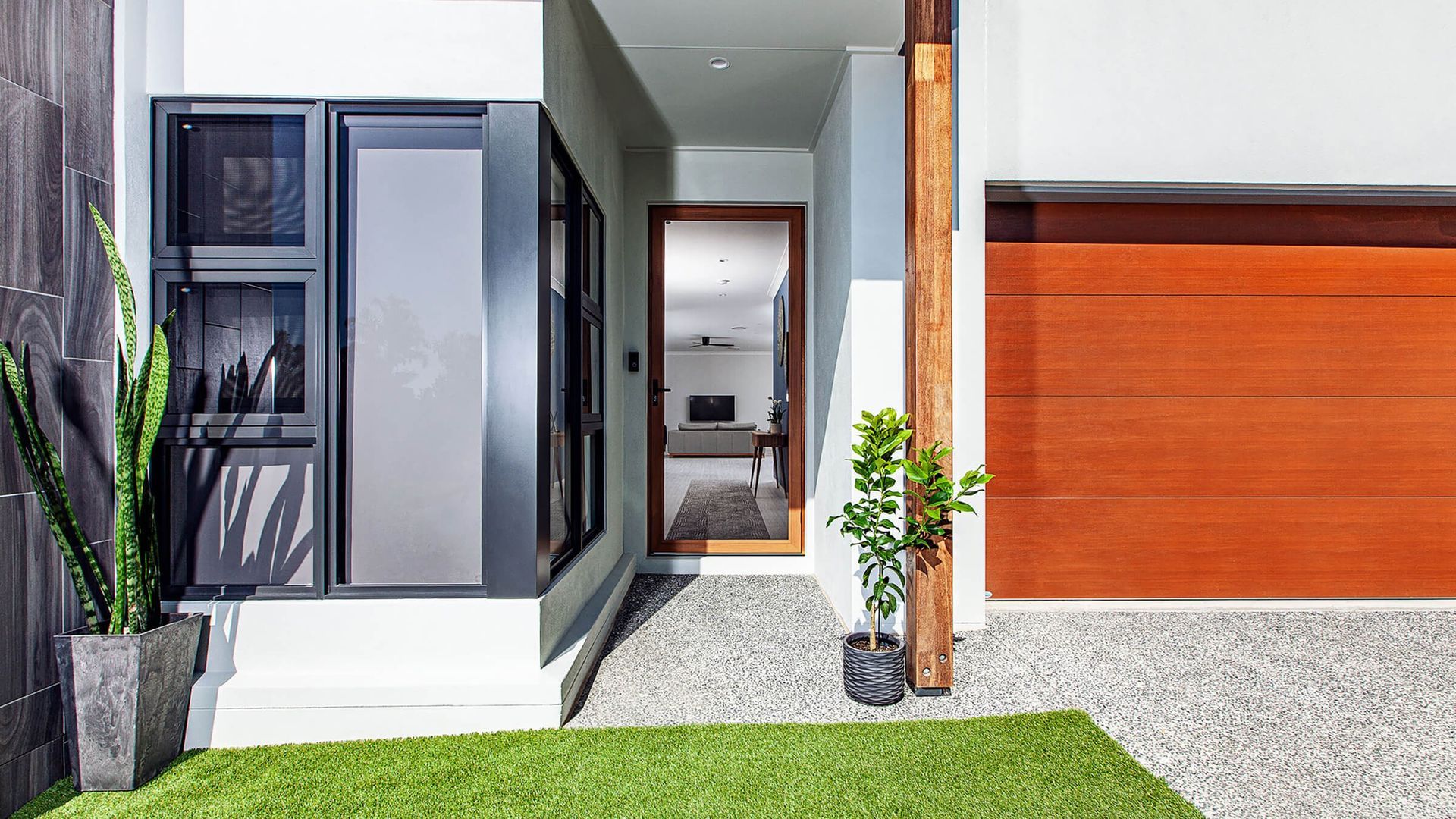 Entryway with wood door, garage door, and gray gravel leading to the front door. Includes a column and potted plants. — Douglass Blinds & Security Screens in Southern Highlands, NSW
