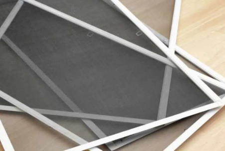 Overlapping white-framed window screens on a light brown surface, with dark gray mesh visible. — Douglass Blinds & Security Screens in Goulburn, NSW