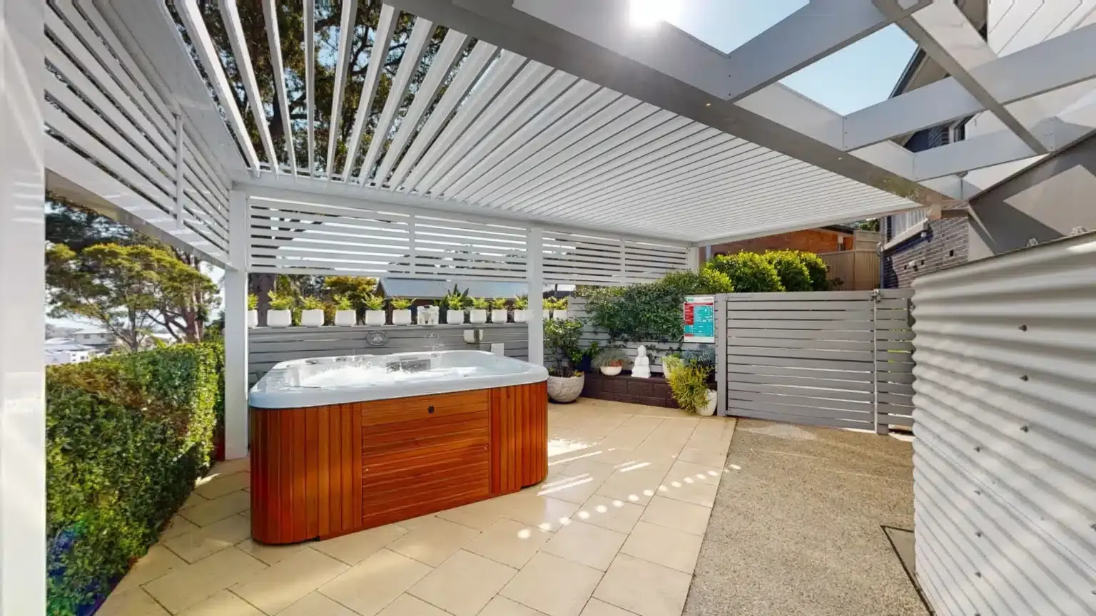 Hot tub under a white pergola on a sunny patio, surrounded by greenery. — Douglass Blinds & Security Screens in Goulburn, NSW
