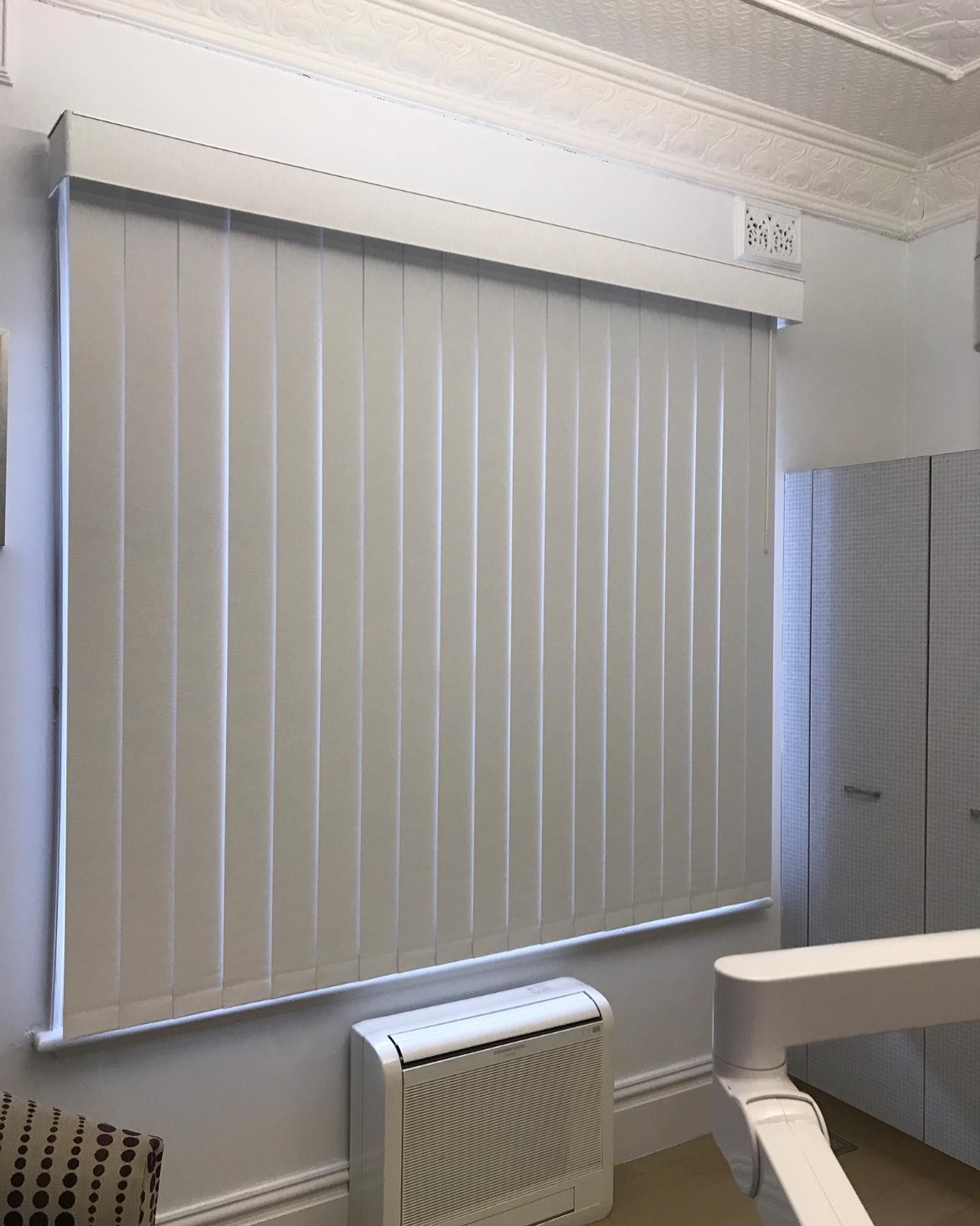 A White Vertical Blind is Hanging on a Window in a Room — Douglass Blinds & Security Screens in Goulburn, NSW
