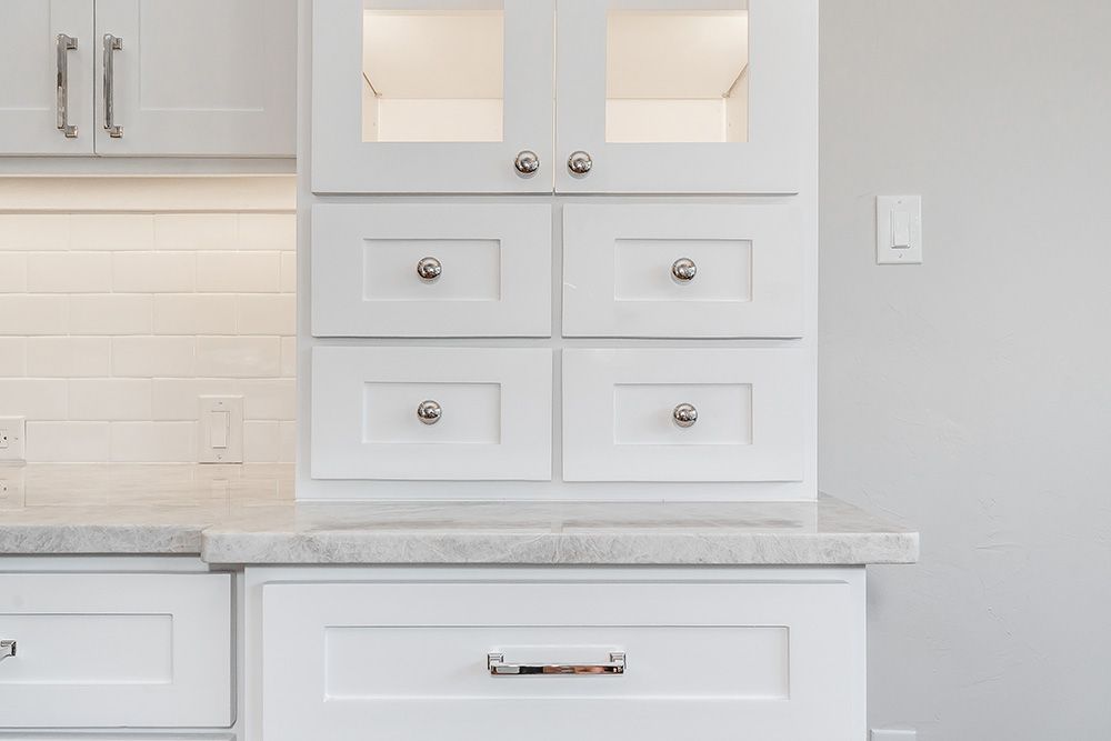 a kitchen with white cabinets and marble counter tops