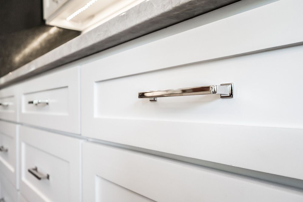 a kitchen with white cabinets and chrome handles