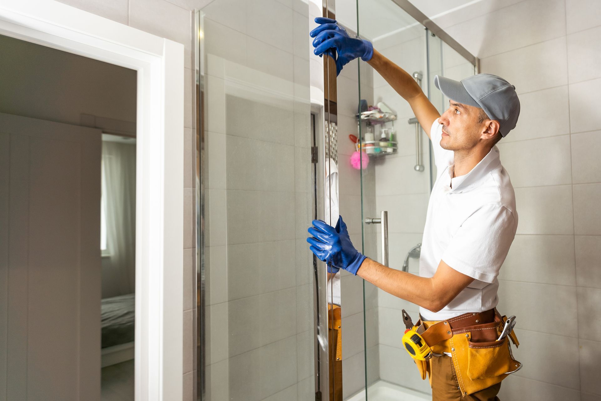 A man in uniform repairs the glass shower screen in the bathroom.