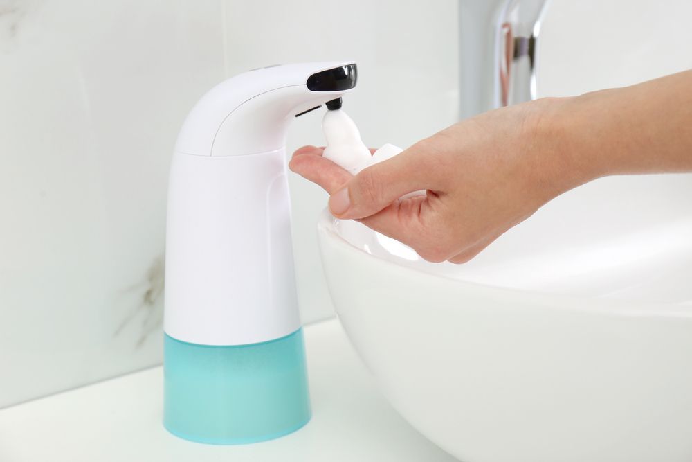 Automatic soap dispenser dispensing foam soap onto a person's hand near a white sink — RWM Cleaning in Deception Bay, QLD