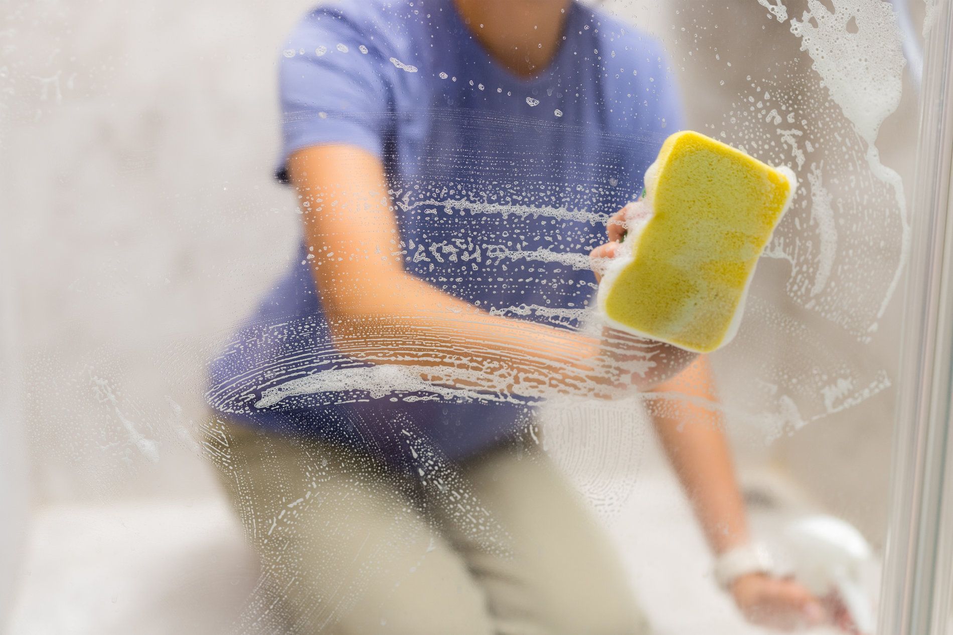 Person cleaning a shower door with a yellow sponge — RWM Cleaning in Deception Bay, QLD
