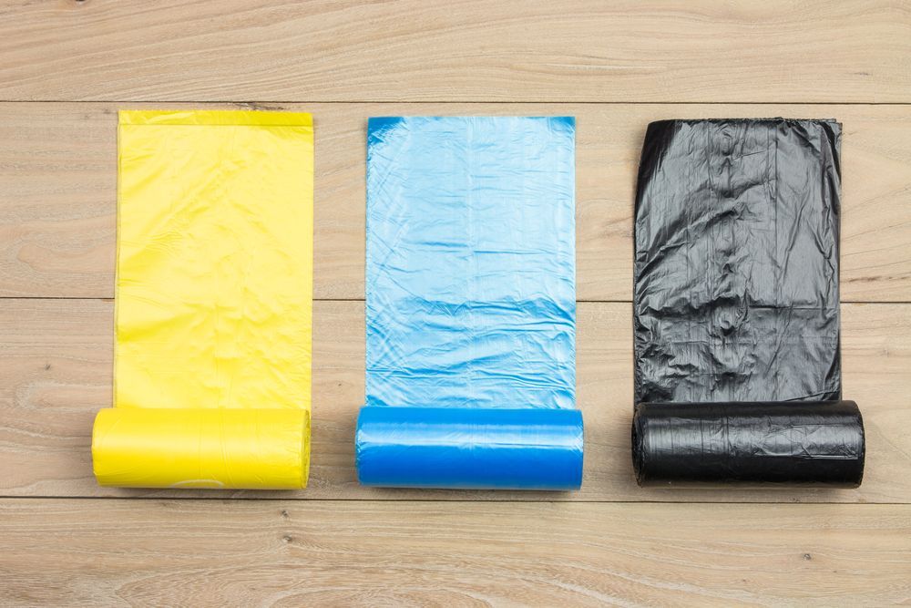 Three rolls of plastic bags: yellow, blue, and black, on a wooden surface — RWM Cleaning in Deception Bay, QLD