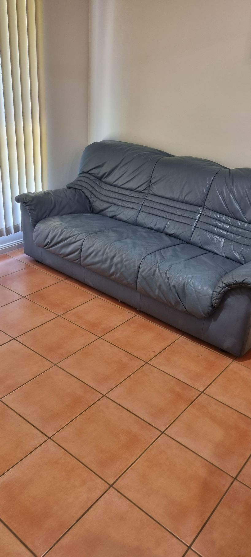 A Worn, Blue Leather Couch Sits in a Room With Brown Tiled Floors — RWM Cleaning in Deception Bay, QLD