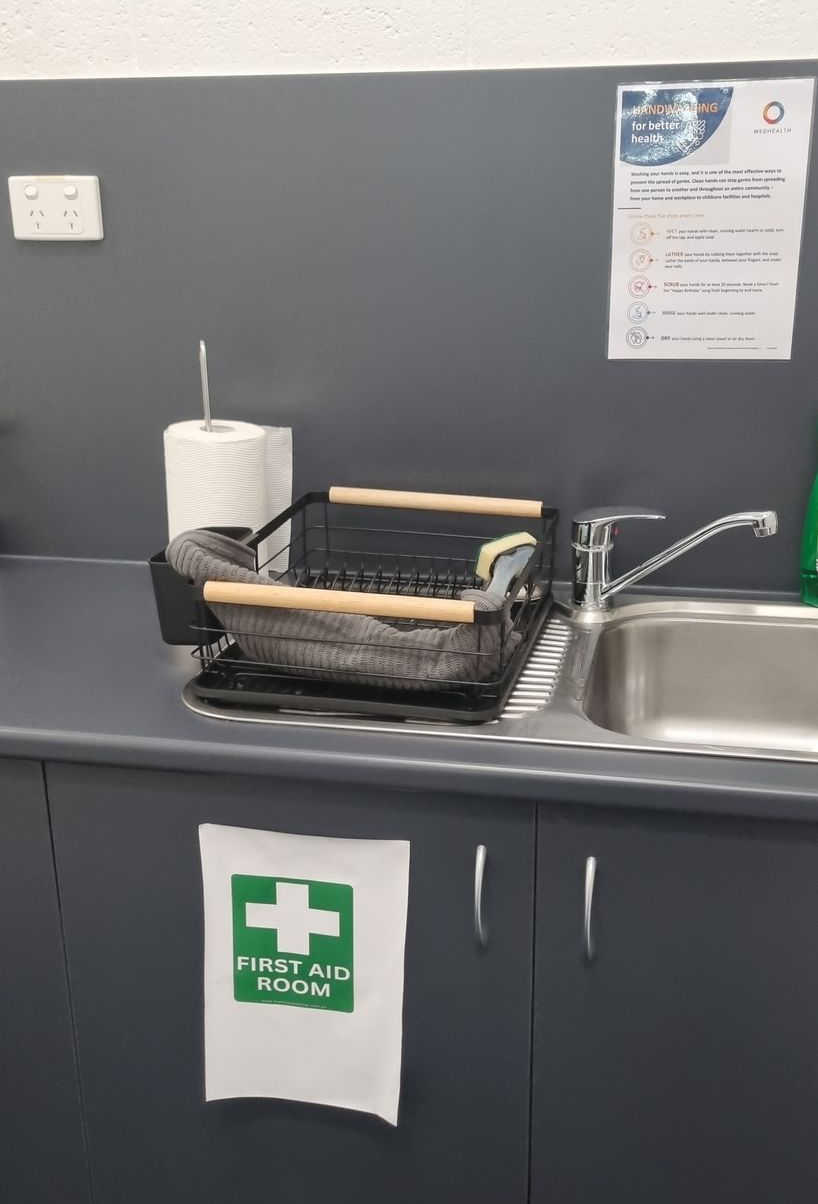 Kitchen sink with drying rack, paper towels, and a first aid sign — RWM Cleaning in Deception Bay, QLD