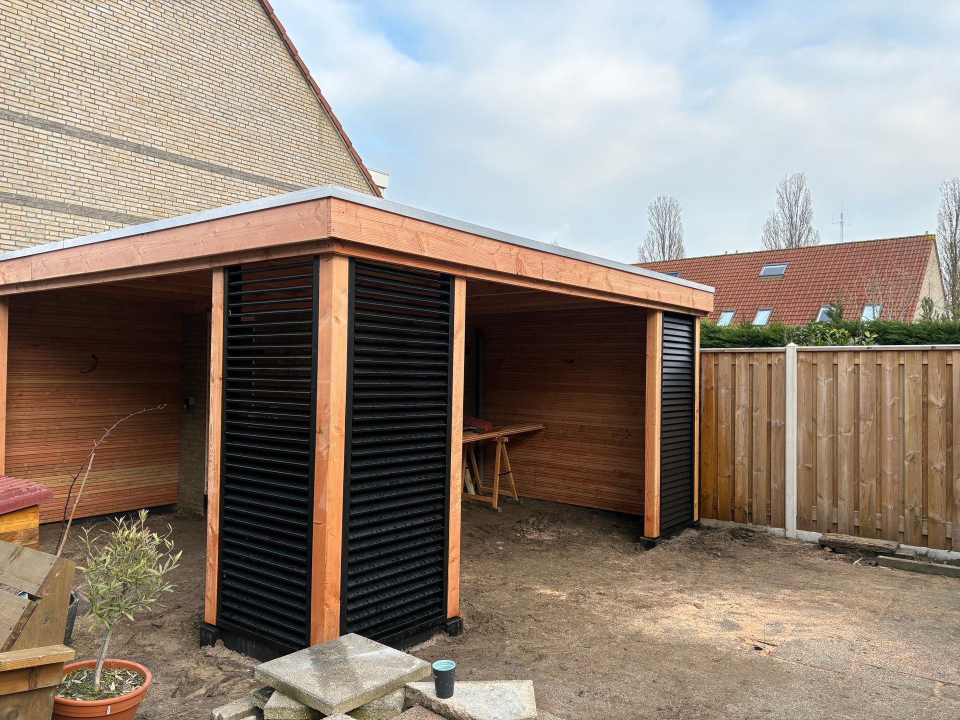 Een houten tuinhuisje met een plat dak en zwarte lattenwanden, gelegen in een omheinde achtertuin.