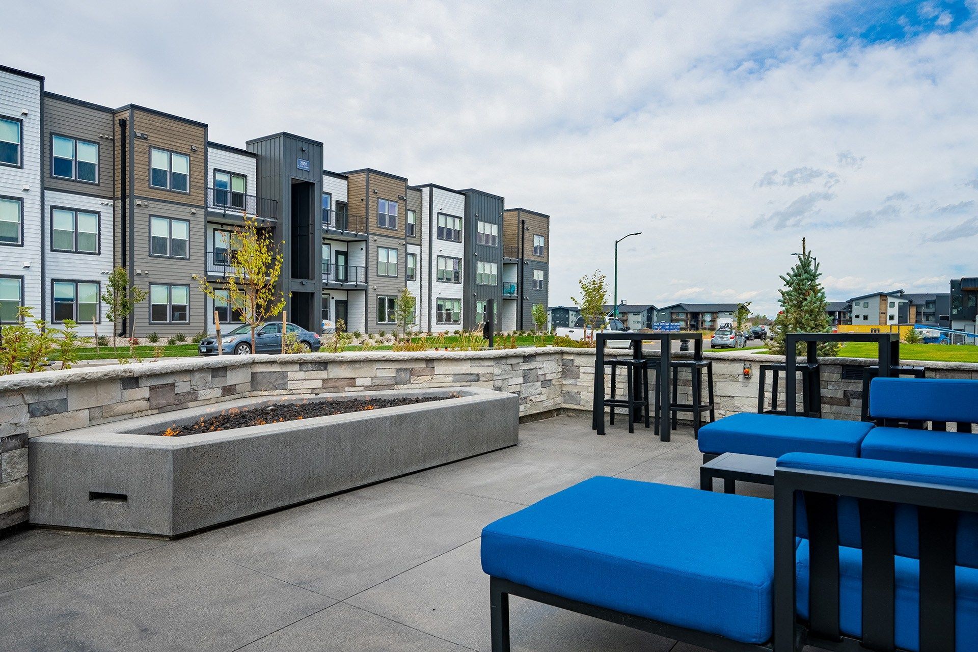 Outdoor lounge area with blue seating, fire pit, and apartment buildings in the background.