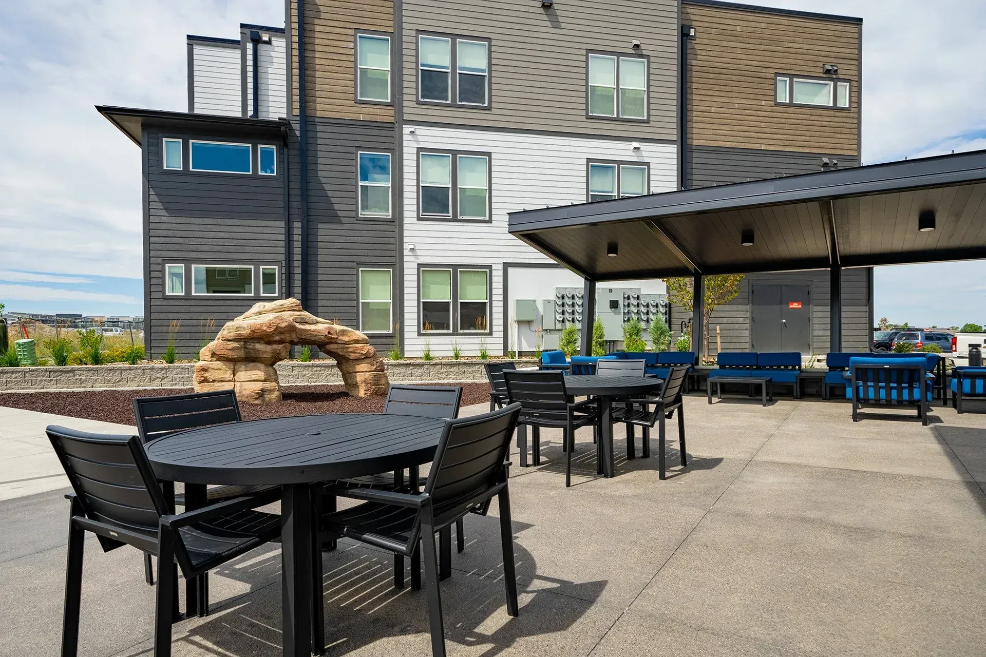 Rooftop patio with black tables, chairs, and a shaded seating area; building in background.