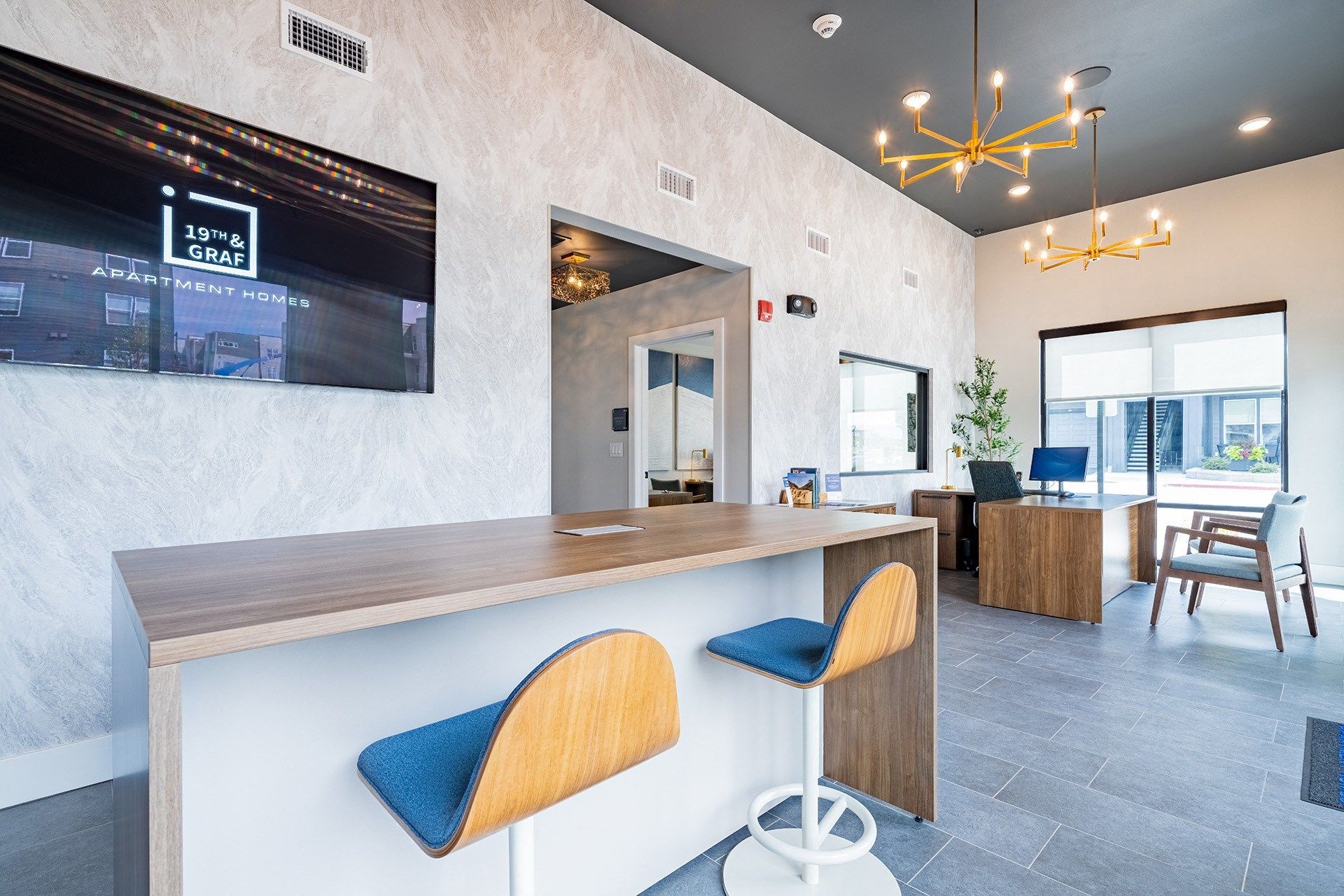 Lobby with a bar, stools, and a desk. TV on the wall. Light fixtures hang from the ceiling.