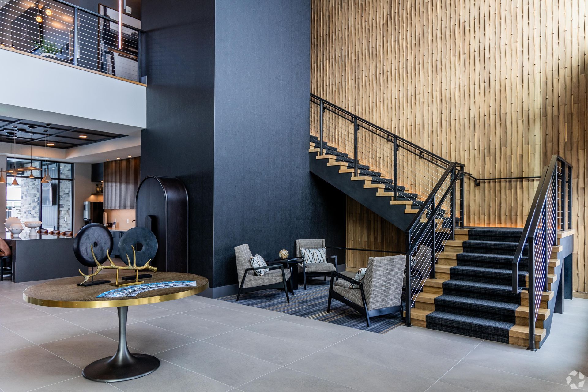 Modern lobby with staircase, seating area, and decorative table. Black and wood tones.