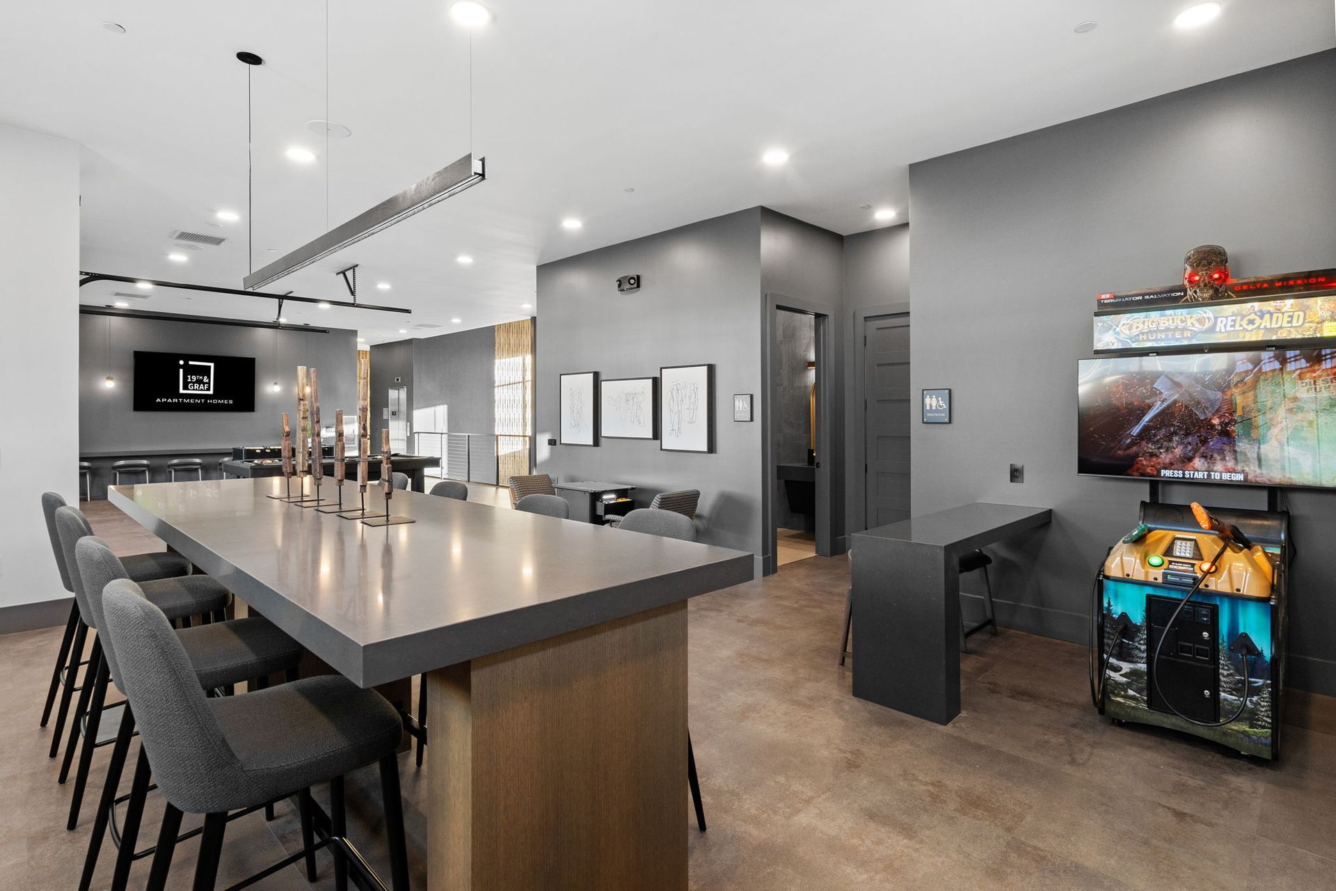 Modern lounge with gray walls, bar seating, and arcade game.