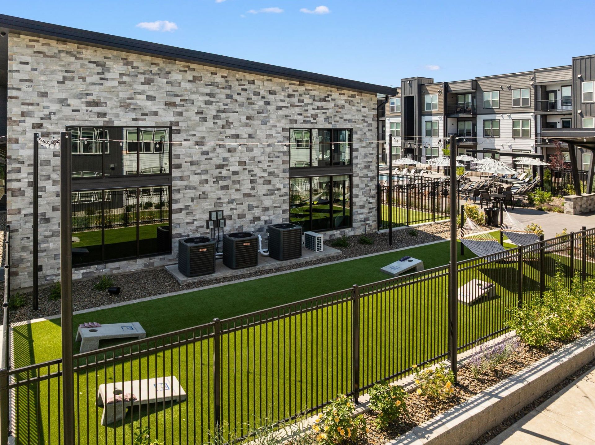 Exterior view of modern apartment building with fenced dog park and green artificial turf.