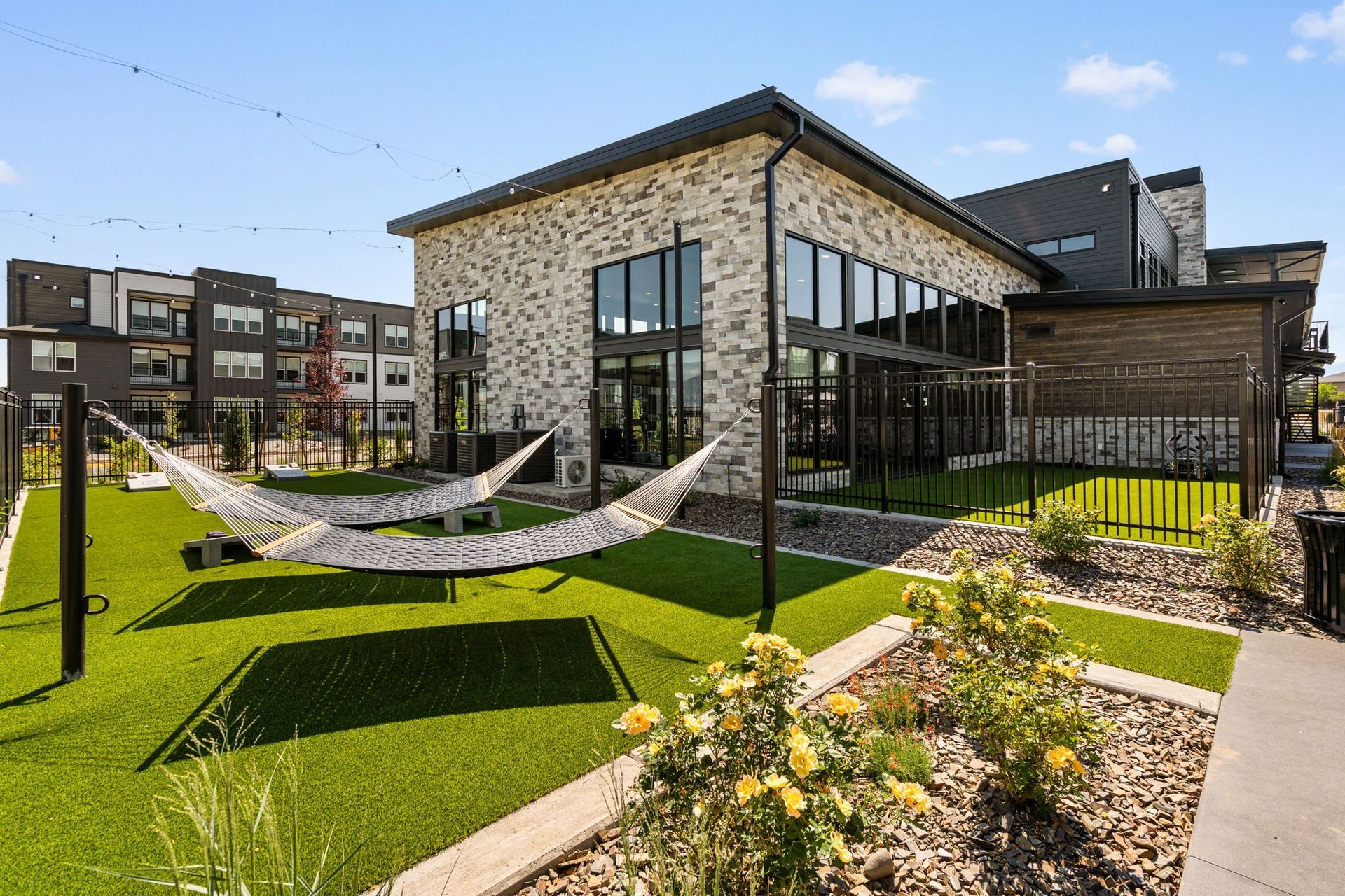 Green lawn with hammocks, a brick building, and apartment complex under a blue sky.