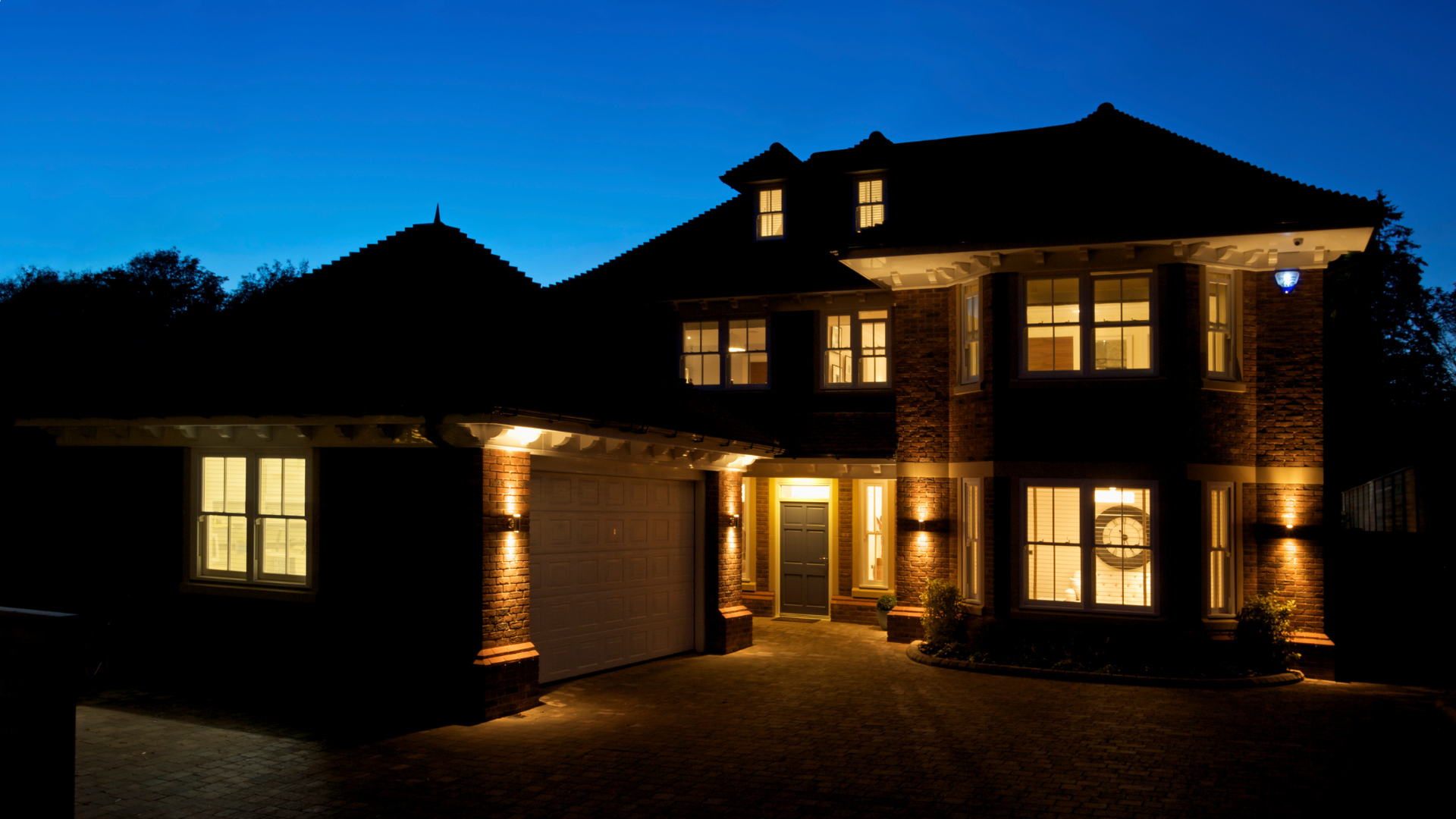 A large house is lit up at night with a blue sky in the background.
