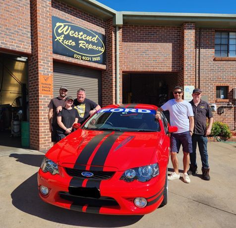 A Group Of Men Standing In Front Of A Red Ford Car — Westend Auto Repairs in Bathurst, NSW