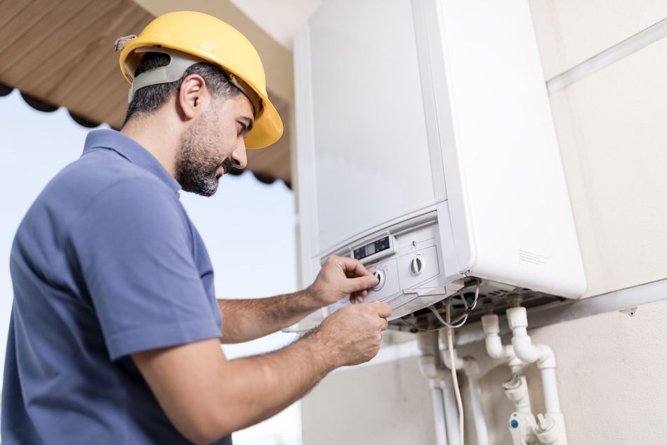 A man wearing a hard hat is working on a boiler.
