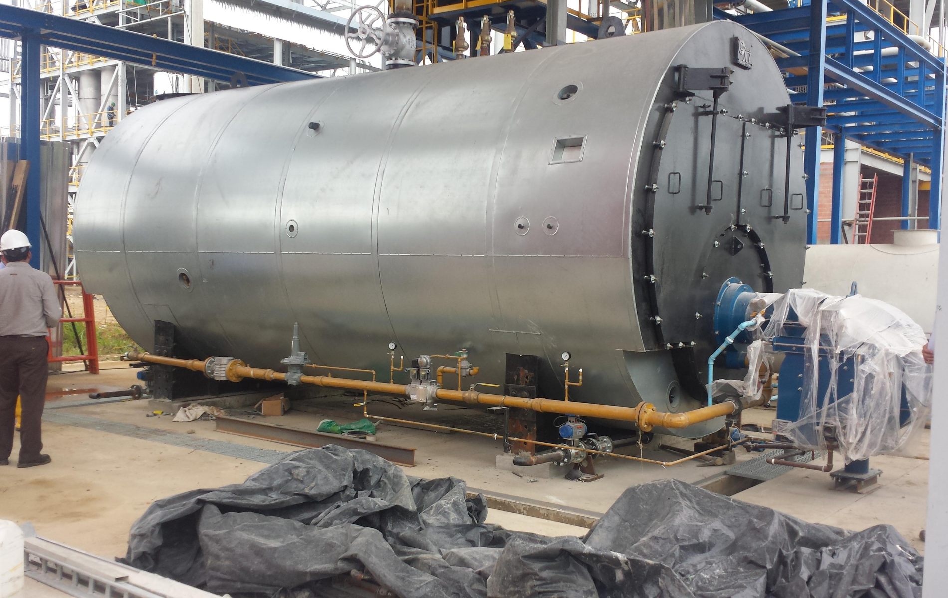 Large, silver industrial boiler in an outdoor setting with workers and equipment.