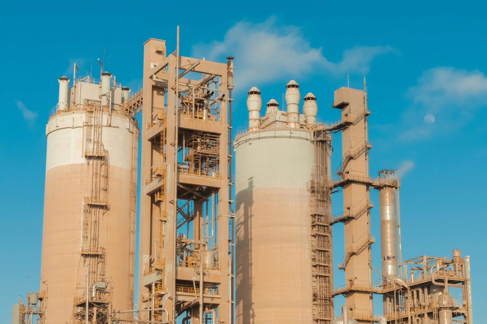 Large beige industrial silos and steel support structures stand against a bright blue sky.