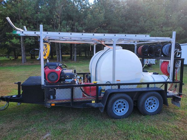 A trailer with a ladder on top of it is parked in a grassy field.