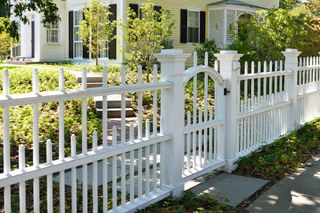 A white picket fence with a gate in front of a house