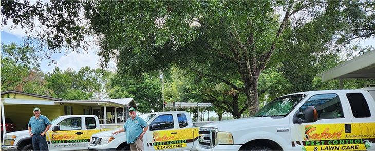 Three white trucks with yellow logos, three men in front, trees and a house in the background.