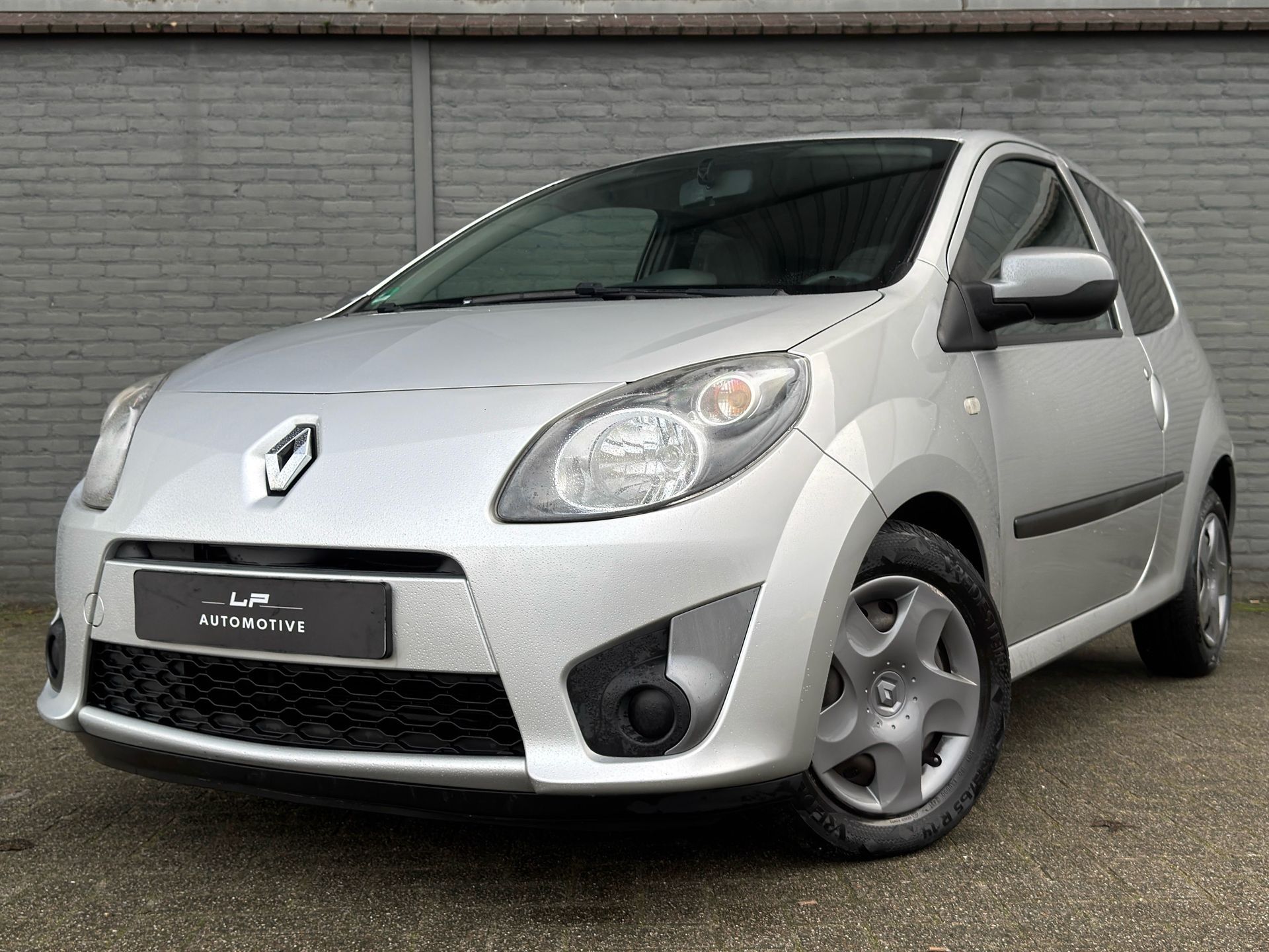 Witte Fiat 500 met zwarte accenten geparkeerd voor een grijze muur.