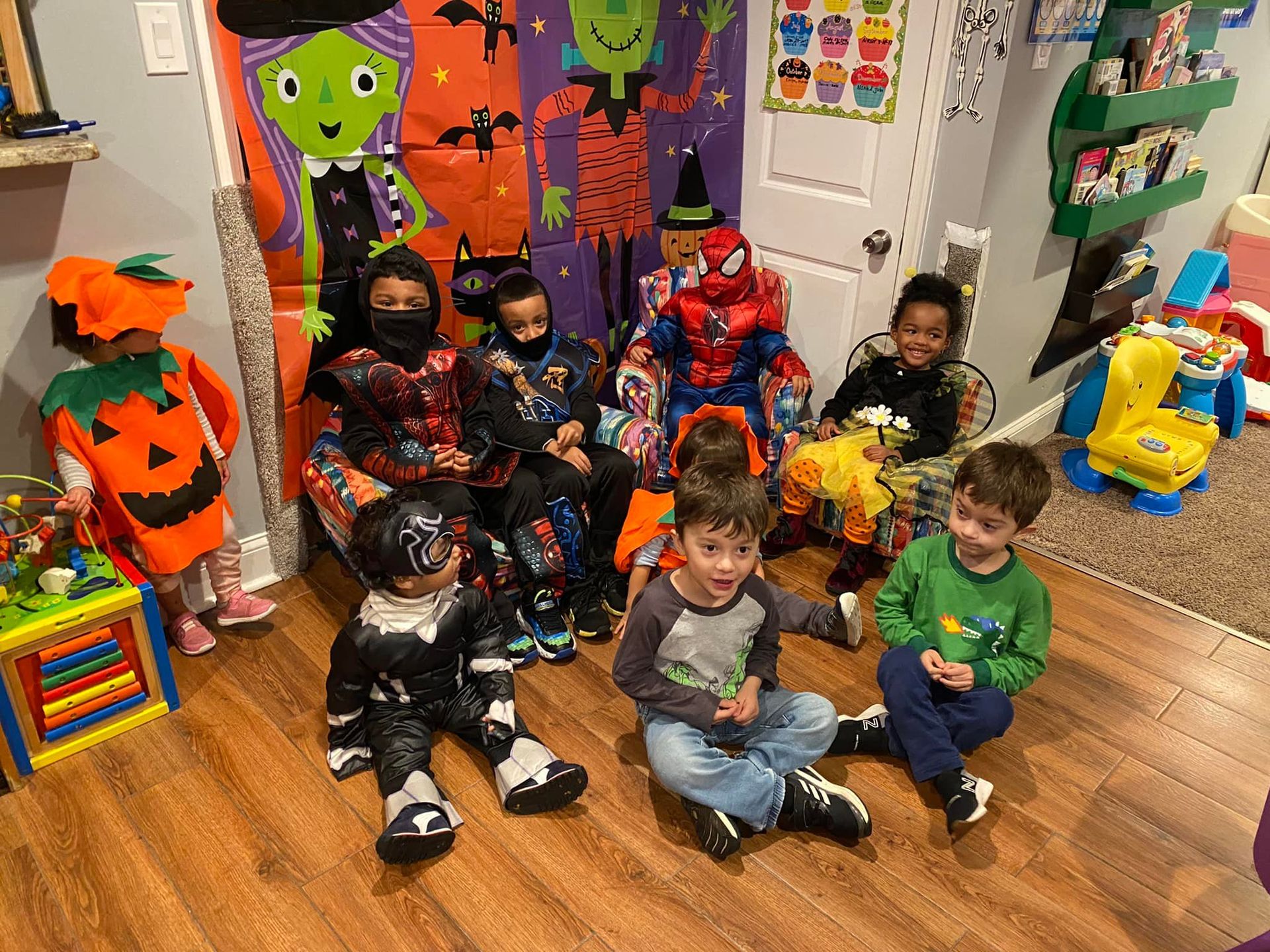Children in Halloween costumes sit in front of decorations, some wearing masks.