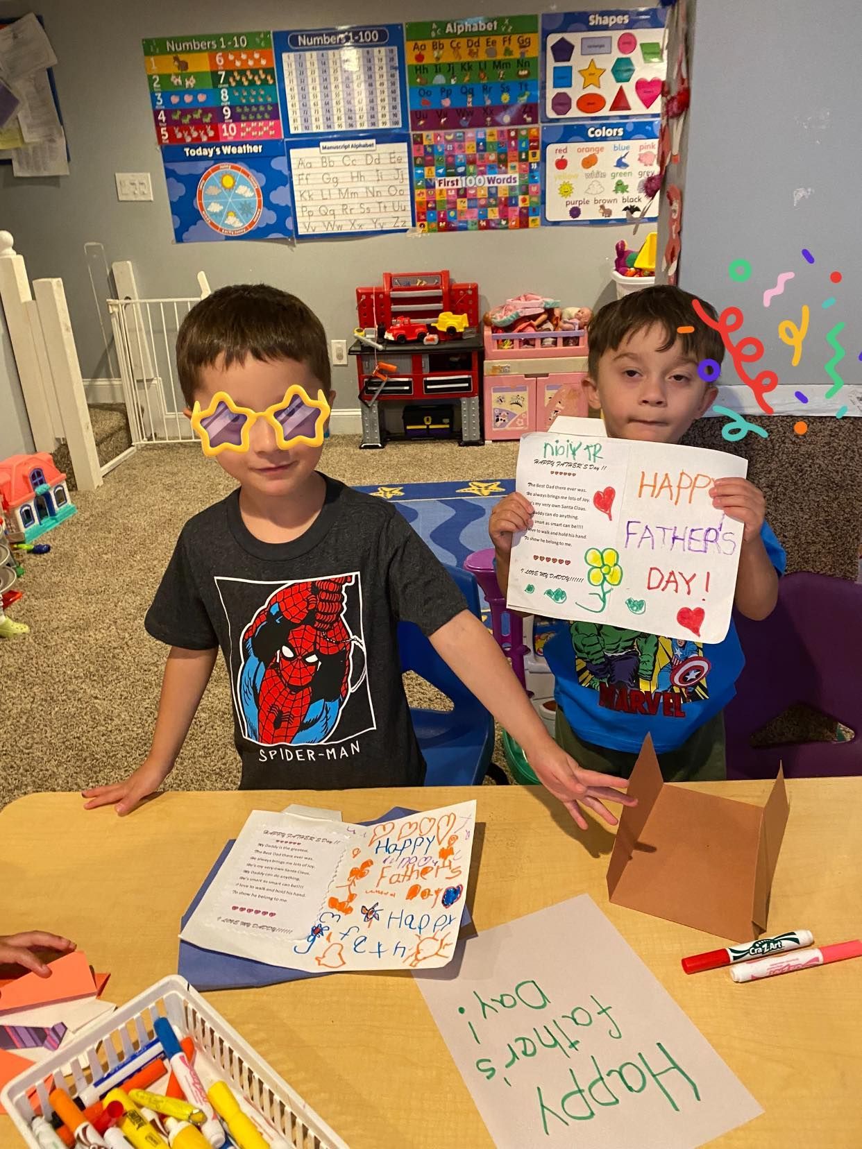 Two boys at a table, making a Father's Day craft and holding a card. One wears star glasses.