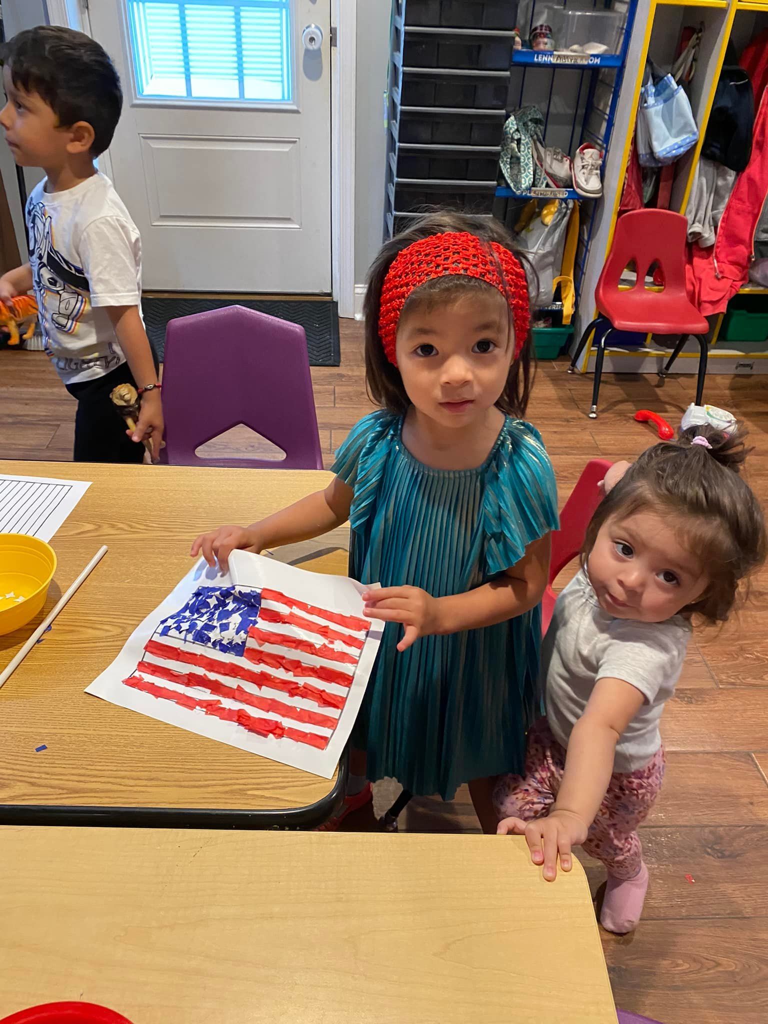Children holding an American flag painting in a classroom.