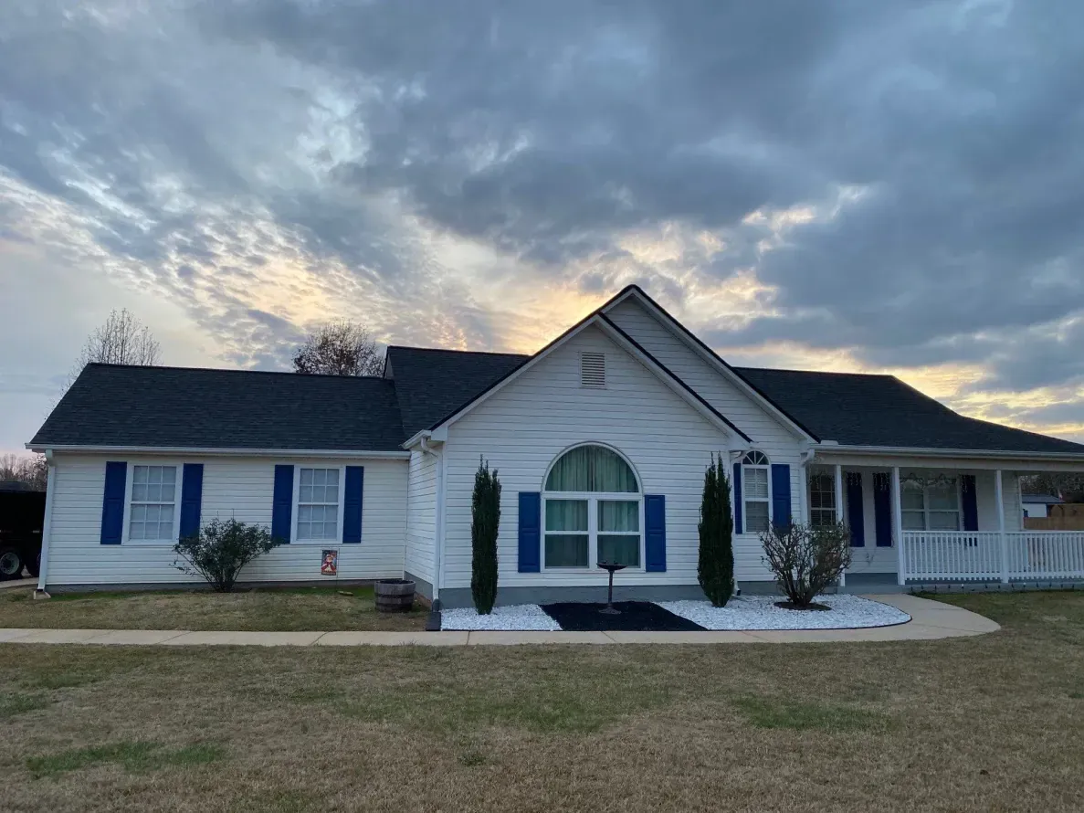 White house with blue shutters, a dark roof, and cloudy sky.