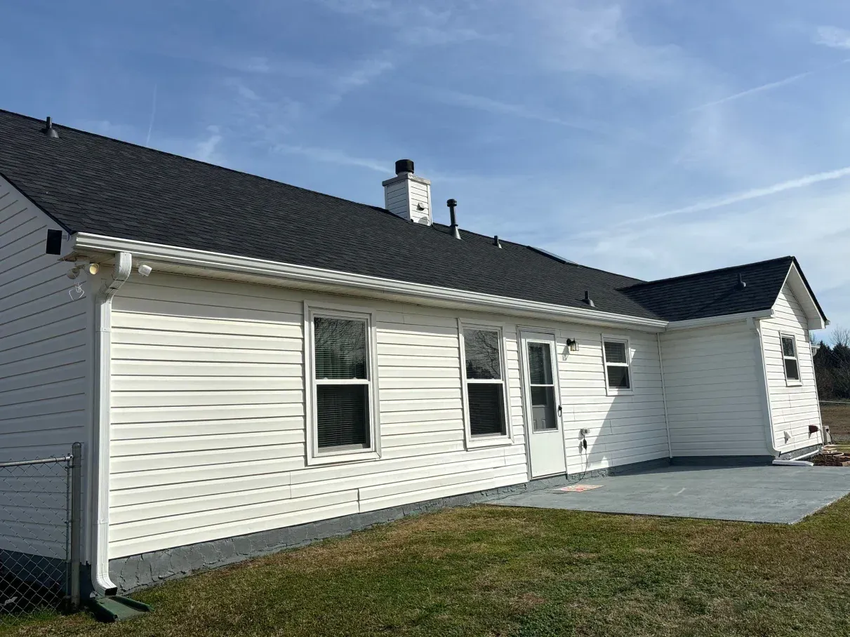 White house with black roof, white siding, windows, door, gray patio, and chimney against a blue sky.