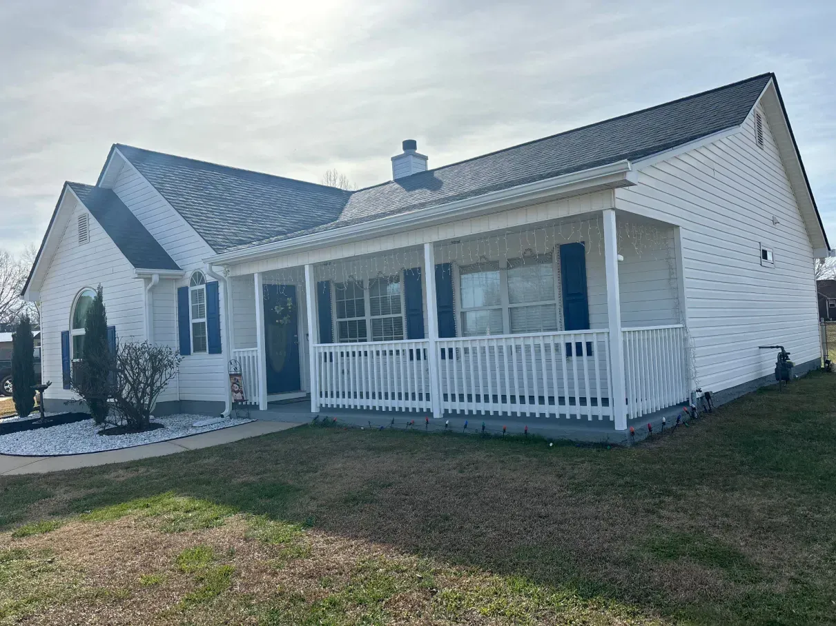 A person digs a trench in a backyard near a small excavator, a tree, and a house.