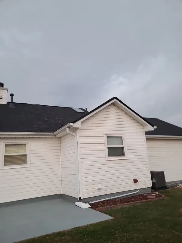 White house with a black roof and a cloudy sky in the background.