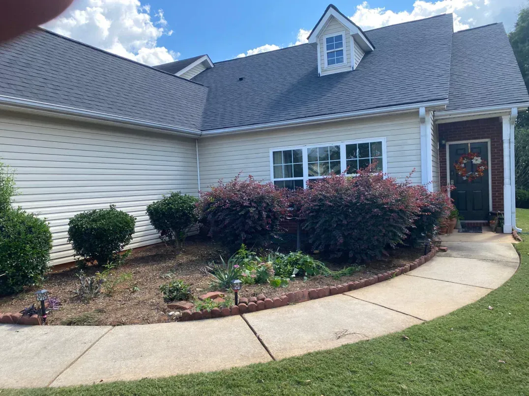 Beige house with dark roof, small dormer, and brick door surround. Landscaping with walkway and green lawn.