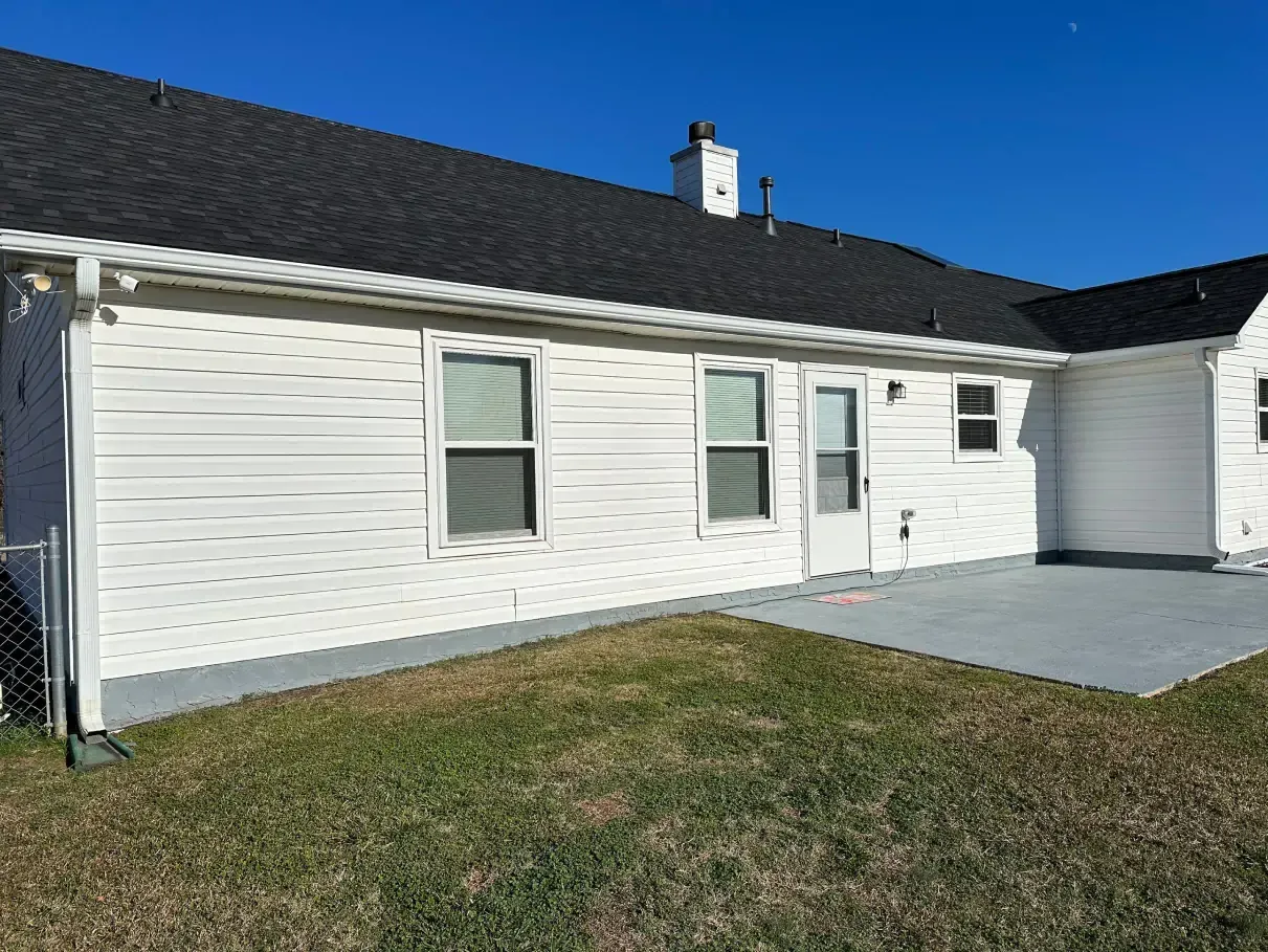 White house exterior with dark roof, windows, and gray patio in a grassy yard.