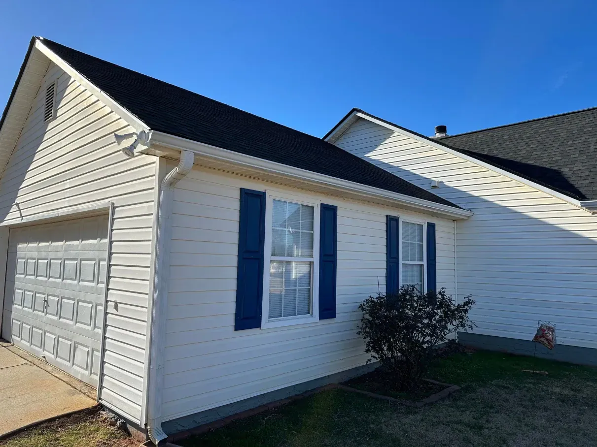White house with black roof, blue shutters, and attached garage on a sunny day.
