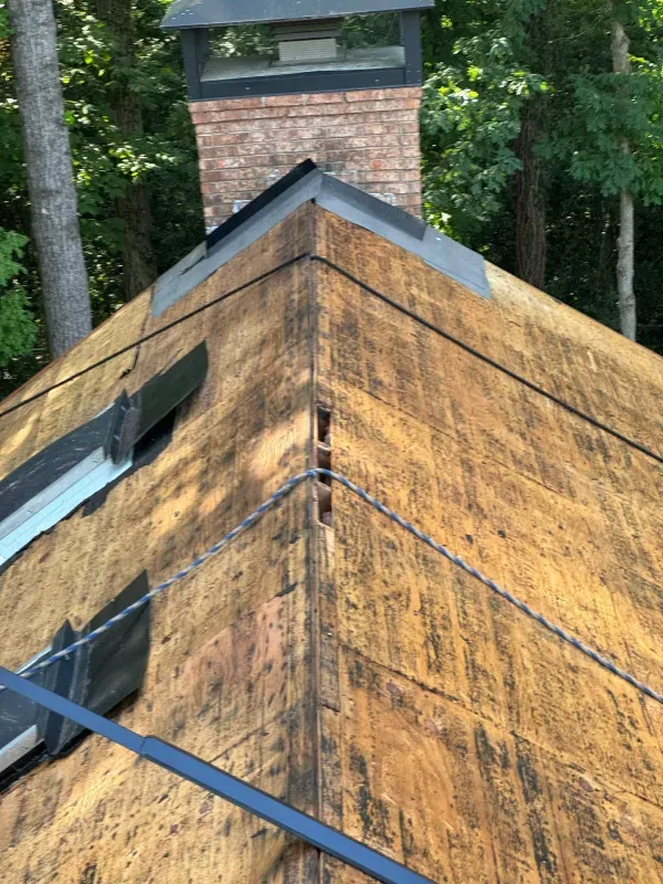 Close-up of a house roof with a brick chimney. The roof is weathered with a metal flashing.