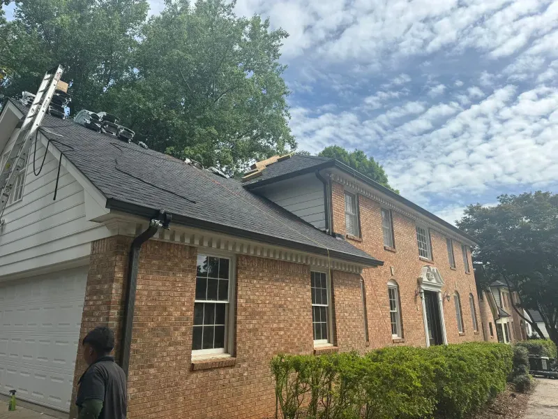 Brick house with roof being worked on, ladder, cloudy sky.
