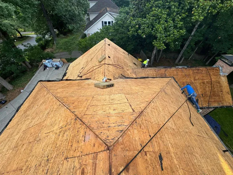 Roofers working on a house roof, removing old shingles. Sunny day, green trees.