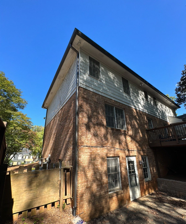 Two-story brick building with white siding, black trim, and a small wooden deck under a blue sky.